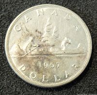 Photo of the reverse side of a 1957 Canadian silver dollar coin featuring the voyageur in a canoe design with year 1957 visible.