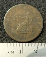 Obverse side of the 1812 Lower Canada Half Penny Tiffin Token showing seated figure holding scales and date at bottom.