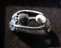 Close-up image of ring front showing black diamond type round stone held in prong setting with adjacent polished silver detail, textured silver band visible.