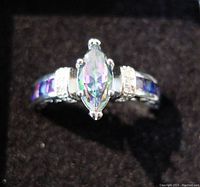 Front view of silver ring with marquise mystic topaz center, diamond accents, and blue inset stones.