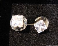 Front view of pair of diamond type fashion stud earrings with clear square-cut stones on a dark background showing prong details.