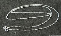 Clear image of the twisted rope-style sterling silver chain laid out coiled on a dark textured surface, showing the lobster clasp and chain details.