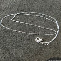 Sterling silver chain necklace with spring ring clasp lying on dark fabric background.