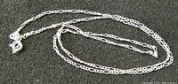 Sterling silver chain necklace on black textured background showing chain links and lobster clasp.