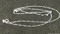 Sterling silver Figaro chain necklace laid out showing the entire chain, folded with clasp visible.