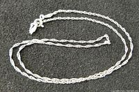 Sterling silver chain necklace shown coiled on black fabric background, highlighting the chain link design and clasp.