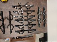 Top down view of 10 black plastic space-saving closet hangers arranged on a table, showing two types of hangers: one with single hooks and multiple holes, and another with double hooks and multiple holes.