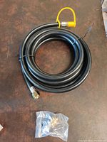 Coiled black rubber hose with metal fittings and yellow safety cap, coiled on brown surface, showing full hose and adapter.