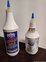 Two bottles side by side: one 32 fl oz Lucas Engine Oil Stop Leak and one 12 fl oz Lucas Transmission Fix Stops Slip, showing front labels and blue caps.
