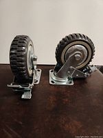 Two heavy duty industrial caster wheels with non-marking rubber tires and brakes displayed on a dark surface.