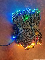 Coiled string of multi-colored LED lights lit up in blue, green, orange, and yellow colors with green wiring.