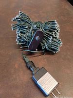 Compact bundle of 300 multi colored LED string lights on green wiring, with rectangular dark brown control switch attached, and power plug visible.