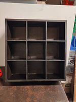 Front view of the 9 compartment shelving unit showing the square grid compartments, finished in black.