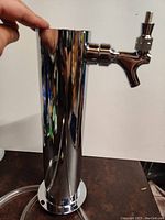 Front and side views of chrome liquid dispenser tap system showing cylindrical main body and dispensing tap with threaded handle.