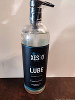 Clear bottle of XESSO Black water-based lubricant with black pump dispenser, front view showing brand and product name.