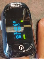 Front view of the pulse oximeter displaying oxygen saturation 98% and pulse rate 85 bpm, showing device in working condition.