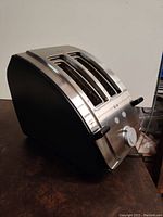 Side angle view of T-fal stainless steel 2-slice toaster on table, showing one lever and control knob.