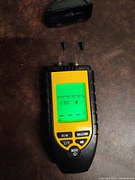 Front view of moisture meter showing screen with moisture percentage, temperature in Celsius, and probes on top.