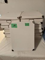 Eleven white rectangular reinforced storage boxes stacked in two rows, showing metal corner protectors and label holders on front.