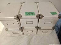 Stack of six white metal storage boxes with metal reinforced corners and front label holders, showing dimensions on green tags.