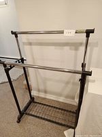 Front view of the 2 bar adjustable clothing rack showing chrome hanging bars, black frame, and bottom metal mesh shelf.
