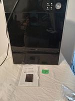 Front view of the black Asept-Air Life Cell 1550 air purifier with control buttons on the top right and owner's manual placed in front.