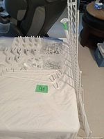 Photo of white ClosetMaid wire shelves laid out on table along with various plastic and metal end pieces, brackets, and wall clips.