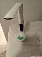 White adjustable desk lamp on a white cloth surface, showing the curved arm and digital touch display on stem.