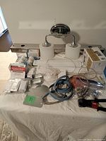 Photo of a variety of electrical supplies including a chrome vanity light fixture with two frosted glass lampshades, electrical wiring, packaged WiFi switches, small electrical components, and a caulking gun tool with a red handle.