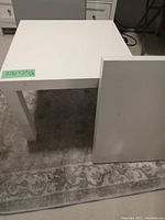 Two white IKEA LACK end tables, one table shown upright; other table top up on floor, showing simple flat surface and legs.