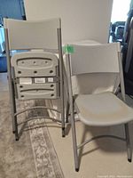 Two white folding chairs, one folded and one unfolded, showing metal frame and plastic seating surfaces.