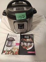 Photo of Instant Pot Duo electric pressure cooker with control panel, recipe booklet and user manual laid flat in front.