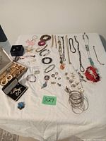 Overview photo of assorted jewelry laid out on white cloth including rings, bracelets, necklaces, and earrings arranged with some boxed jewelry displayed.