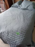 King size bed made with light blue textured bedspread and two matching pillowcases on headboard