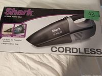 Photo of the Shark 12 Volt handheld cordless vacuum box showing the product image and advertised features such as 12 Volt power and bagless dust cup.
