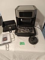 Sur La Table air fryer open view showing basket, skewers, rotisserie basket, and manual on table.