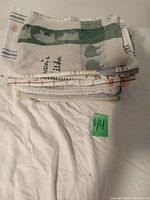 Stack of 21 assorted tea towels featuring various patterns including green and beige cat silhouettes and striped designs