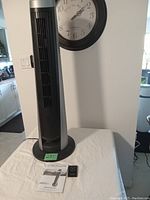 Full view of the Bionaire tower fan with remote and manual placed on table under a wall clock.