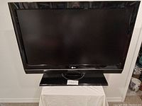 Full front view of the LG 37-inch flat screen TV set on a stand covered with white cloth.