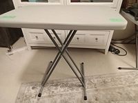 Front view of the folding TV table showing X-shaped silver-gray metal legs and gray rectangular tabletop.