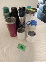 Photo showing eight water bottles and tumblers of various materials and colors arranged on a white cloth.