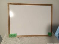 Rectangular white board with a smooth white surface and wooden frame placed against a wall.