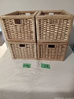 Front-facing view of four wicker baskets stacked in a 2x2 formation showing woven natural tan wicker material and rectangular cut-out handles on two opposite sides.