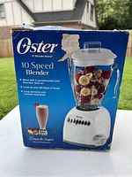 Box of Oster 10 Speed Blender front view showing the blender image with fruit inside jar and product details.