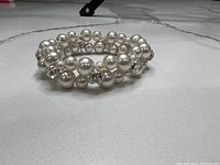 Triple strand faux pearl bracelet with clear crystal accent beads, coiled design on a tiled surface.