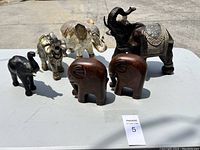 Overhead view of all 7 decorative elephant figurines arranged on an outdoor table showing variety in size, material, and finish.
