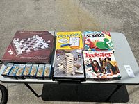 Full lot of games displayed on a table including chess set, Pictionary, Sorry!, Twister and Tumbling Tower stacks.