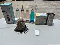 Wide shot of all items on a table including glass bottle, drink dispensers, salt lamp, boxed bowls, and utensil holder.