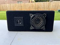 Front view of black rectangular speaker showing a small tweeter and larger woofer with protective metal grill.