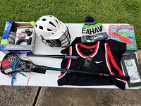 Overview of all sports equipment on table including helmet, lacrosse sticks, Nike jersey, beanie, sprinkler, and bicycle starter items.